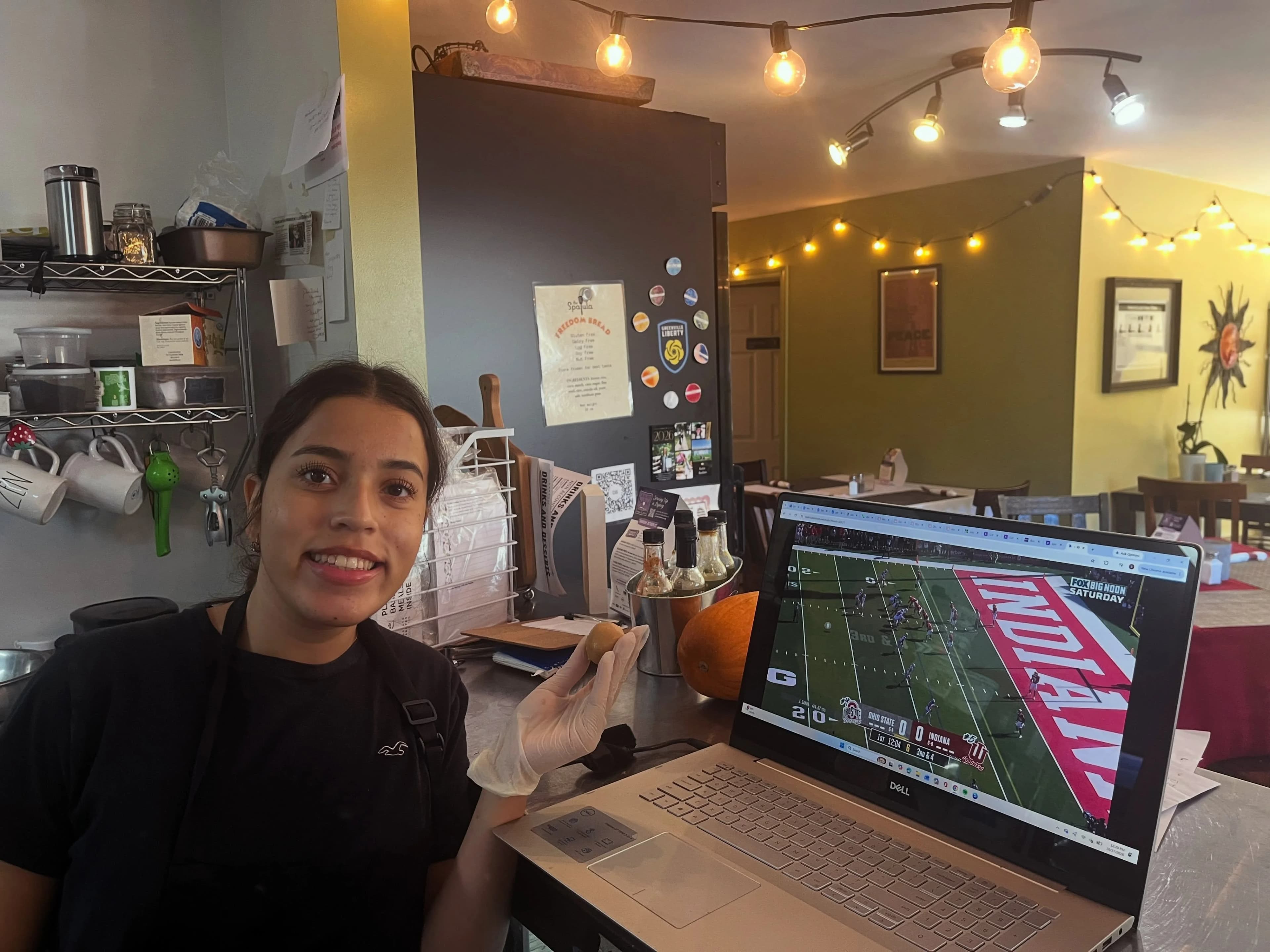 A person in an apron behind Sun Belly’s cafe counter beneath string lights